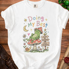 White t-shirt with a frog on a mushroom and signs reading "Slow Progress" and "Still Progress".
