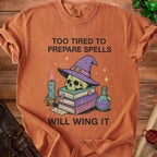 T-shirt with skull wearing witch hat, books, candle, potion, and text "Too tired to prepare spells, will wing it".