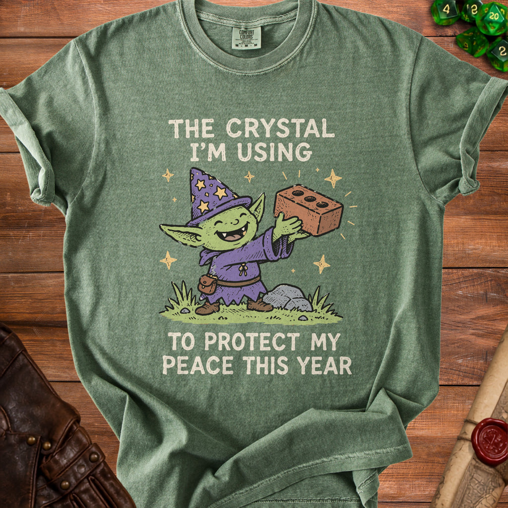 Green t-shirt with a cartoon goblin wizard holding a brick with text "The crystal I'm using to protect my peace this year".