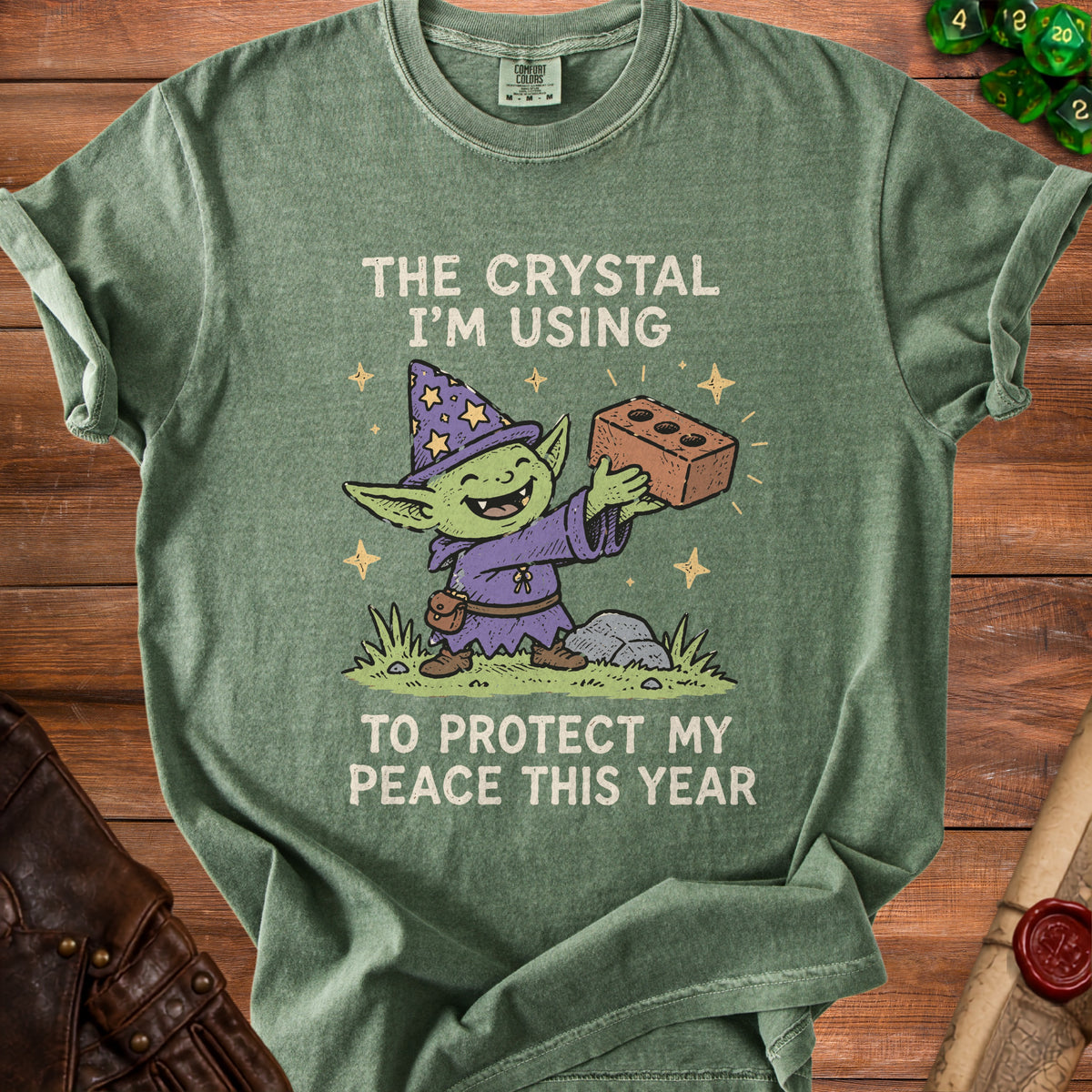 Green t-shirt with a cartoon goblin wizard holding a brick with text "The crystal I'm using to protect my peace this year".