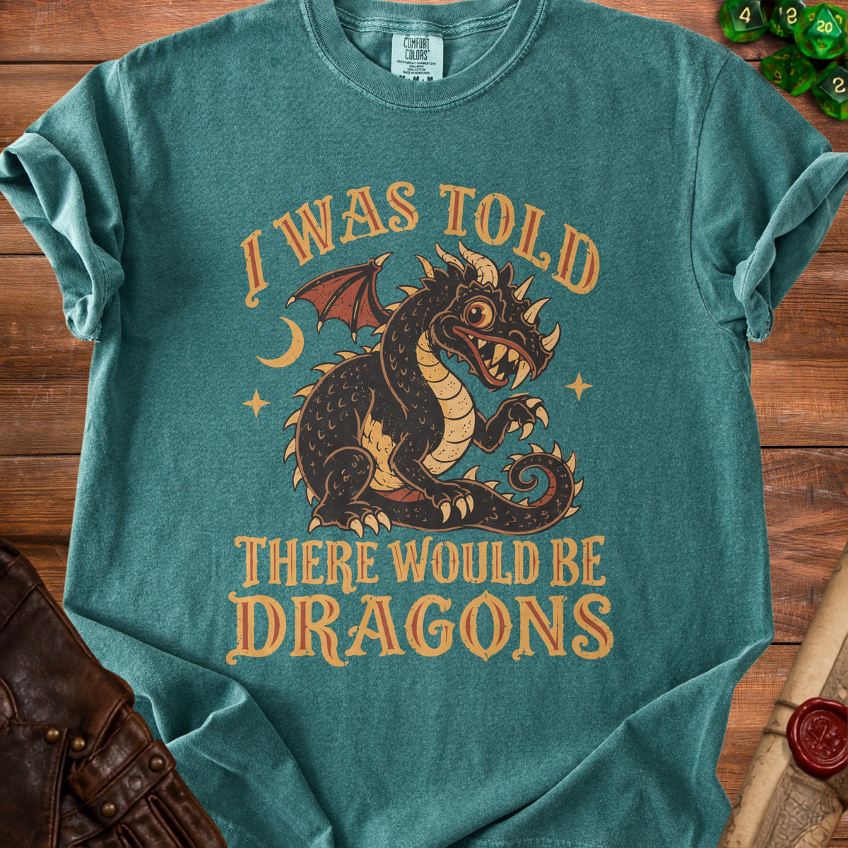 Teal t-shirt with a black dragon graphic and text "I WAS TOLD THERE WOULD BE DRAGONS".