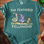 Green t-shirt with a graphic of three birds in fantasy costumes and the text "THE FEATHERED FELLOWSHIP".