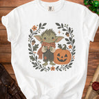 White t-shirt with a cute goblin holding a heart-shaped d20, surrounded by fall leaves.