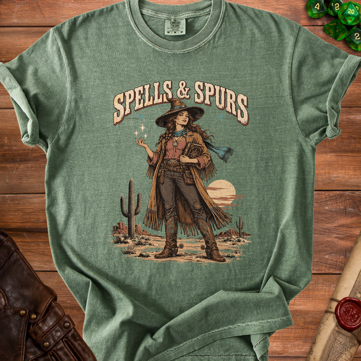 Green t-shirt featuring "Spells & Spurs" text and a desert witch illustration.