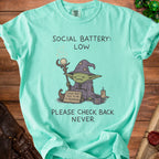 Mint green t-shirt with a goblin wizard saying "Social Battery: Low. Please don't talk to me I'm recharging."