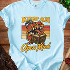 Light blue t-shirt with "Keep An Open Mind" text and a monster chest reading a book.