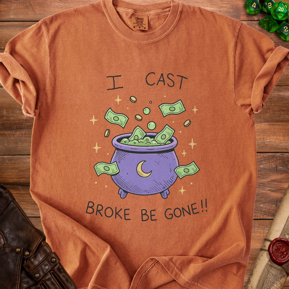 Orange t-shirt with a graphic of a cauldron overflowing with money and stars, saying "I CAST BROKE BE GONE!!".