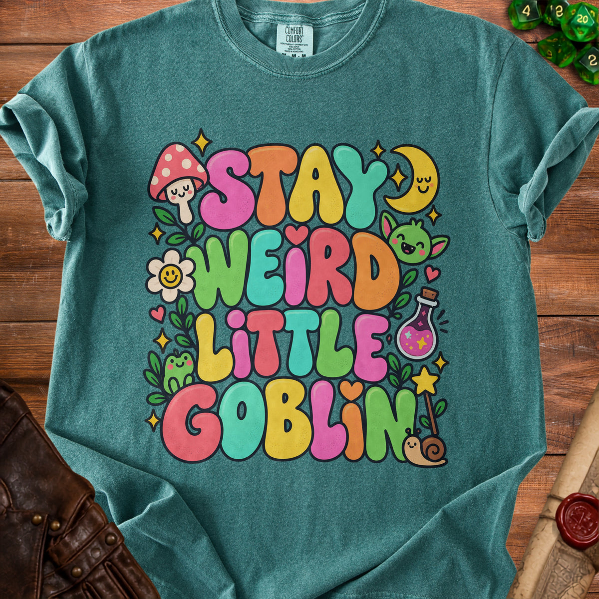 Teal t-shirt with colorful "Stay Weird Little Goblin" text and whimsical illustrations.