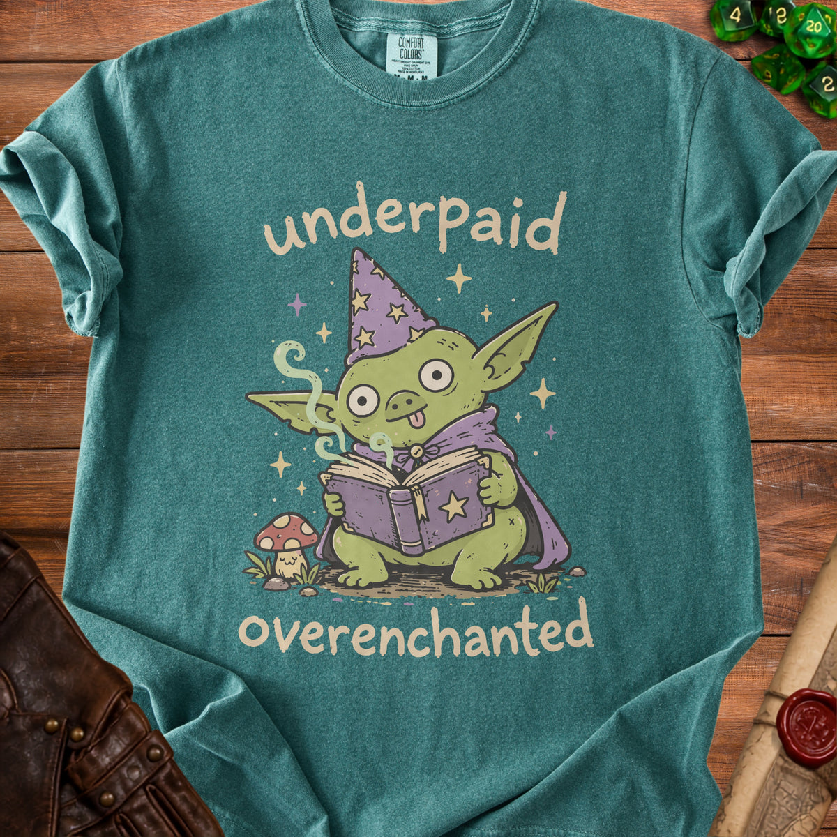 Green t-shirt with goblin wizard reading book and text "underpaid overenchanted".