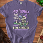 Purple t-shirt graphic featuring a skeleton drinking water with text "Suffering? Don't forget to drink water! Please Stay Hydrated While You Suffer."