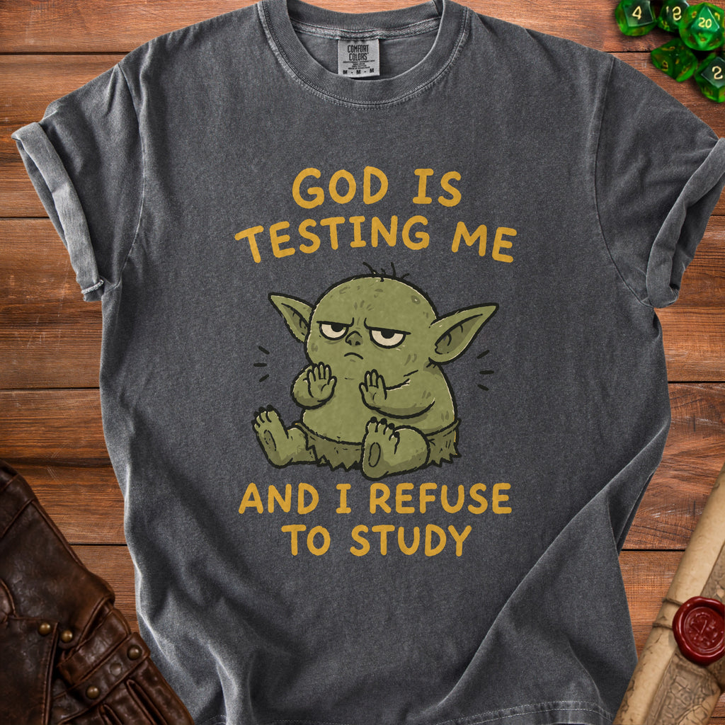 Dark gray t-shirt with a cartoon green creature and text "GOD IS TESTING ME AND I REFUSE TO STUDY".