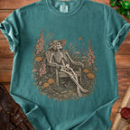 Skeleton in a straw hat relaxing in a chair surrounded by flowers and butterflies.