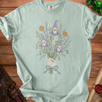 Skeleton hand holds bouquet of pumpkins and gnome skull flowers, tied with blue ribbon.