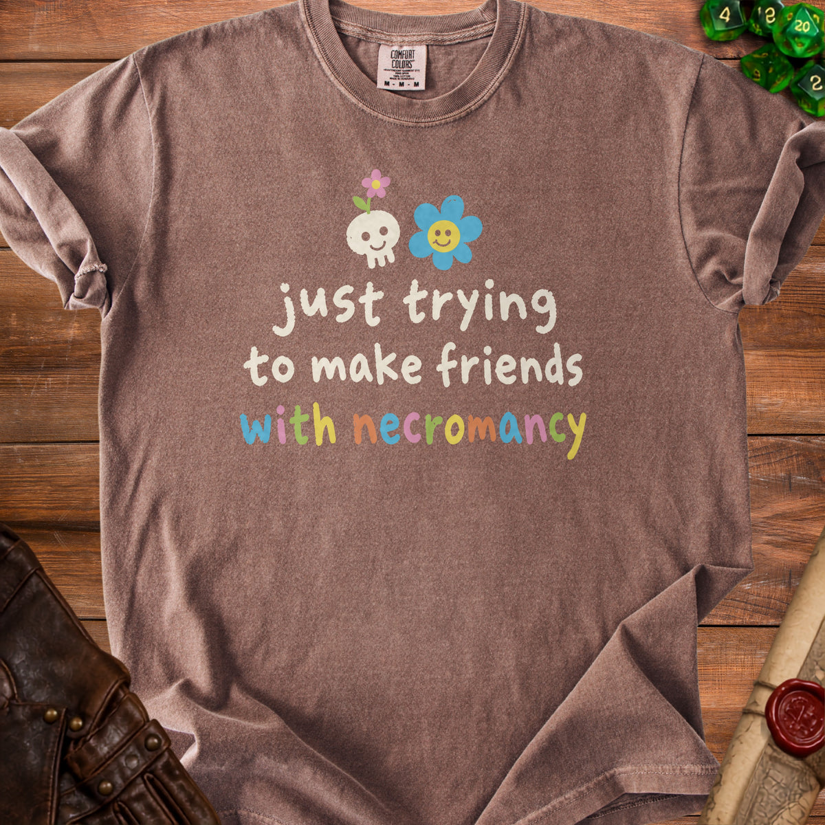 Brown t-shirt with "just trying to make friends with necromancy" graphic and skull and flowers.