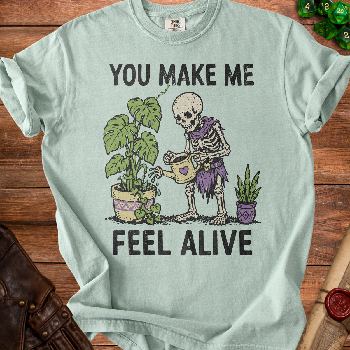 Skeleton watering plants with text "YOU MAKE ME FEEL ALIVE".