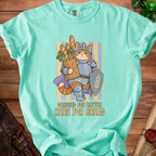 Turquoise t-shirt graphic of a cat knight holding bread and a shield, text says "Dressed for Battle Here for Bread".