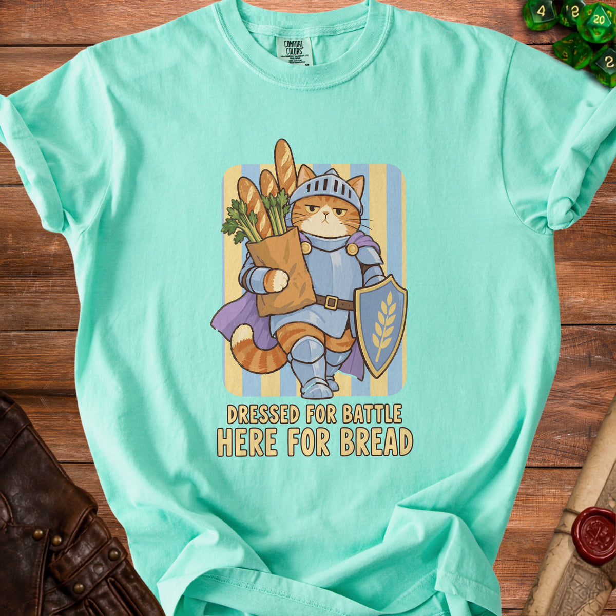 Turquoise t-shirt graphic of a cat knight holding bread and a shield, text says "Dressed for Battle Here for Bread".