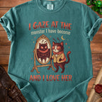 Teal t-shirt with cartoon cat looking in mirror at monster, text reads "I gaze at the monster I have become and I love her".