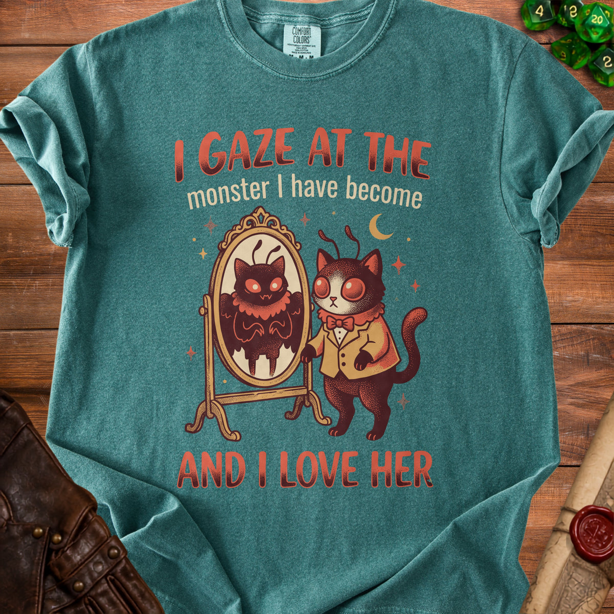 Teal t-shirt with cartoon cat looking in mirror at monster, text reads "I gaze at the monster I have become and I love her".