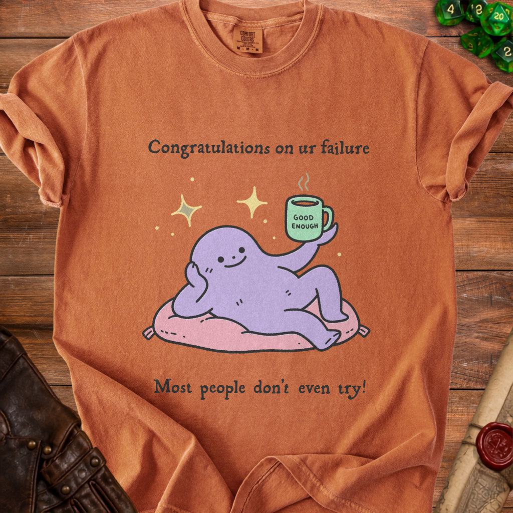 T-shirt with purple character holding a coffee mug that says "Good Enough" and text "Congratulations on ur failure."