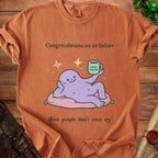 T-shirt with purple character holding a coffee mug that says "Good Enough" and text "Congratulations on ur failure."