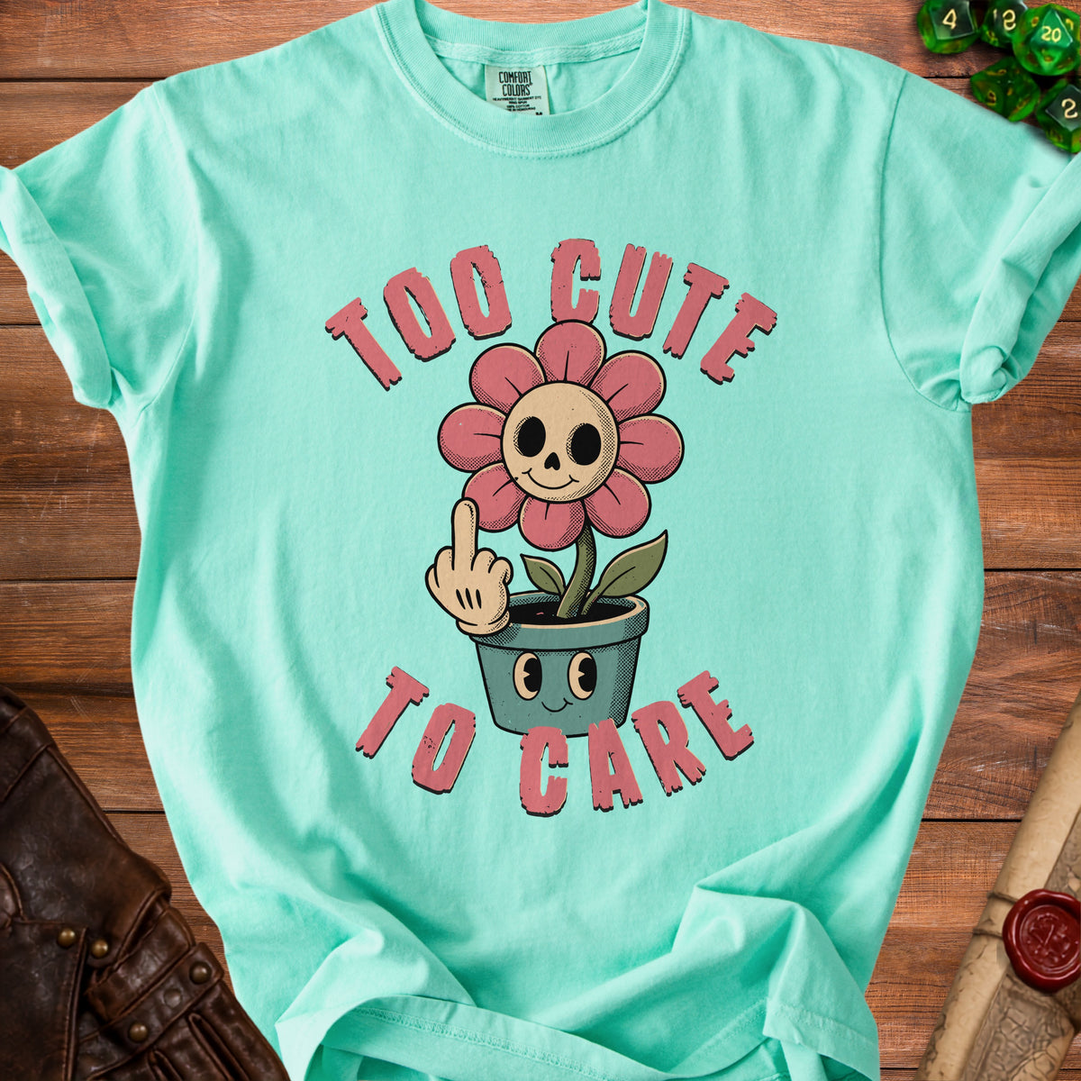 Aqua t-shirt with cartoon skull flower giving middle finger, text "Too Cute To Care".