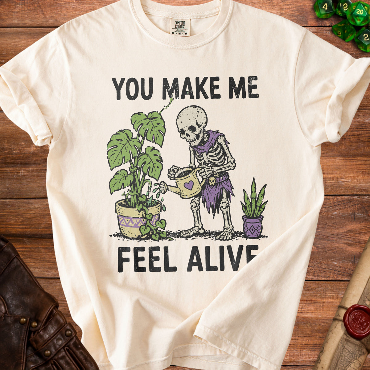 Cream t-shirt with skeleton watering plants, reads "YOU MAKE ME FEEL ALIVE."