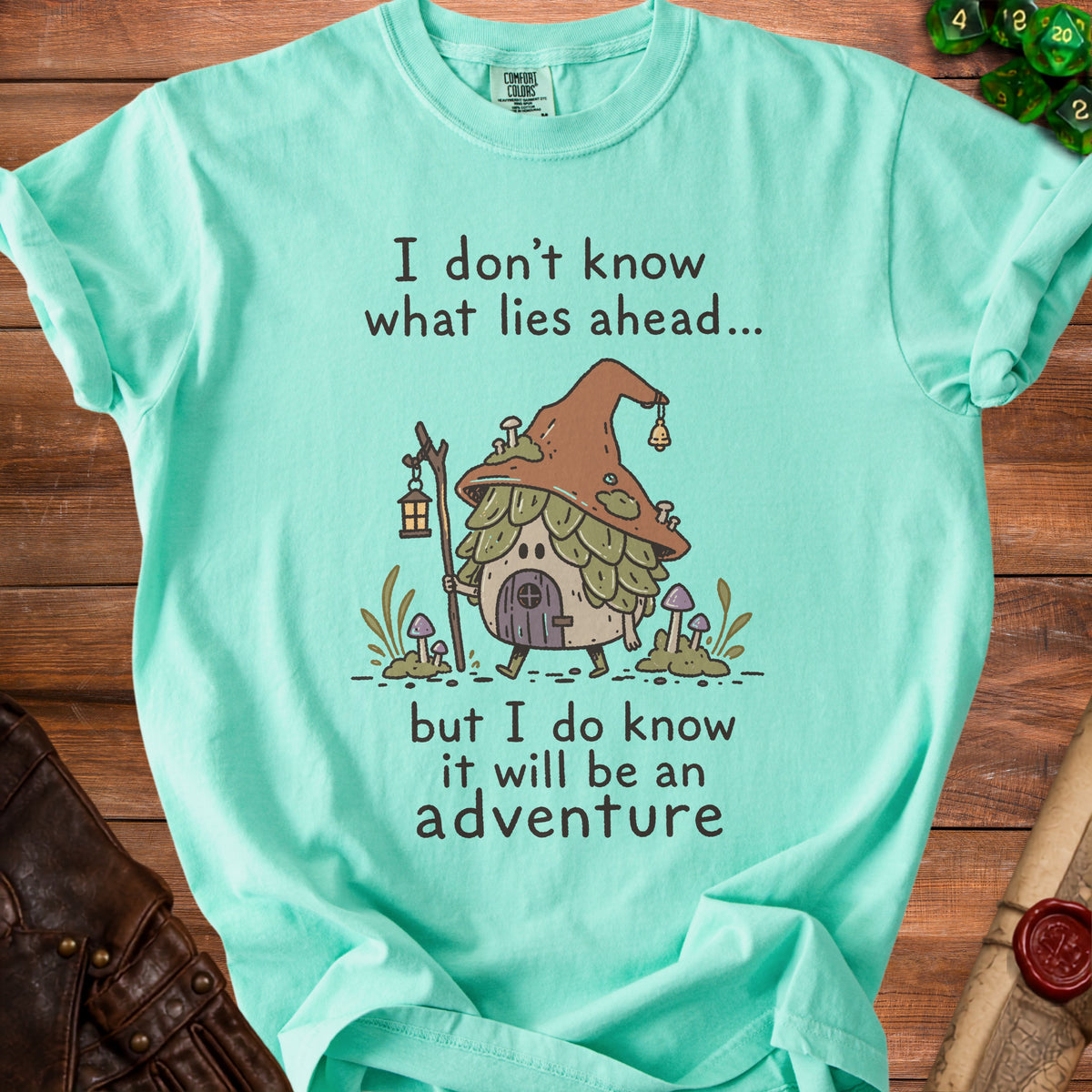 Aqua t-shirt with illustration of a mushroom house and text "I don't know what lies ahead... but I do know it will be an adventure".