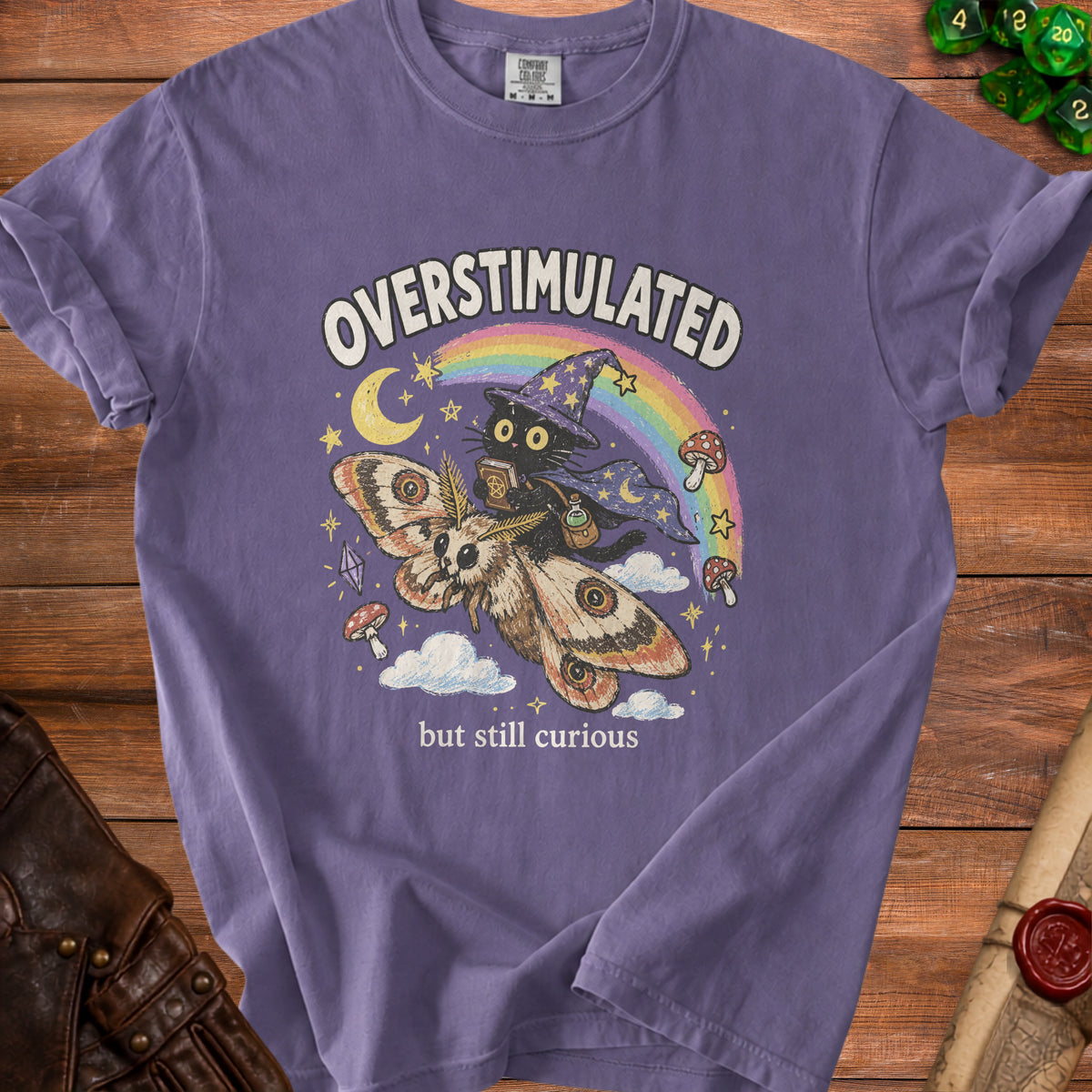 Purple t-shirt with a black cat in a wizard hat riding a moth, saying "overstimulated but still curious".