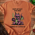 Orange t-shirt with a pink dragon wearing sunglasses and holding coffee. "Hop up out the bed summon my coffee on."