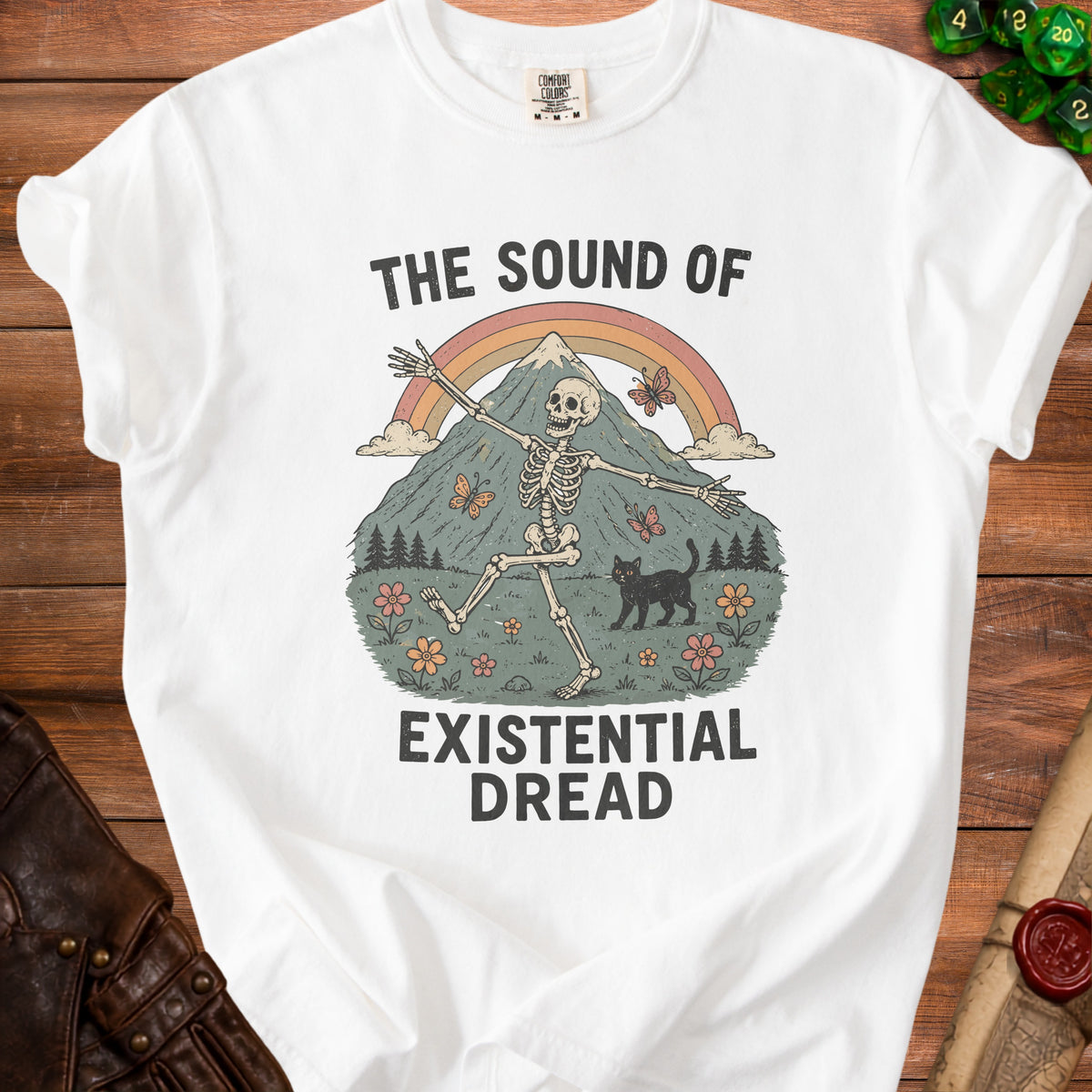 White t-shirt with skeleton, black cat, mountain, rainbow, and butterflies graphic.