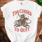 White t-shirt with graphic of goblin riding opossum, text "Too Cursed To Quit".