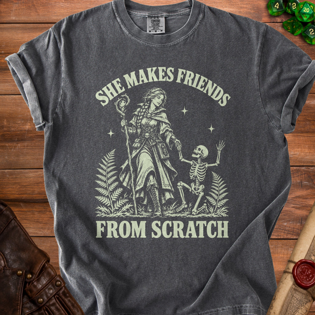 Dark grey t-shirt with graphic of woman and skeleton, text "SHE MAKES FRIENDS FROM SCRATCH".