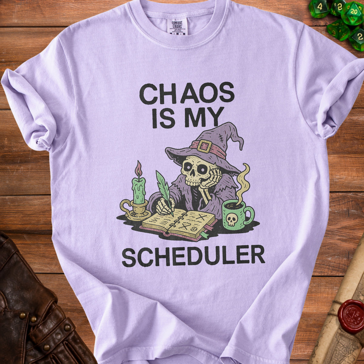 Lilac t-shirt with skull writing "Chaos Is My Scheduler" and a skeleton wizard.