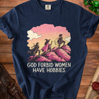 Dark blue t-shirt featuring three women adventuring on pink hills with the text GOD FORBID WOMEN HAVE HOBBIES.