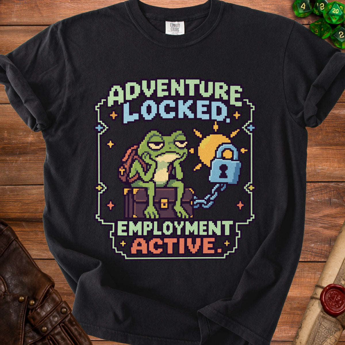 A black t-shirt features a pixel art graphic of an unenthusiastic frog sitting on a chest, with the text "ADVENTURE LOCKED, EMPLOYMENT ACTIVE."