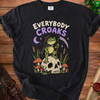 A grim reaper frog sits on a skull with mushrooms and reeds, with "EVERYBODY CROAKS" text.
