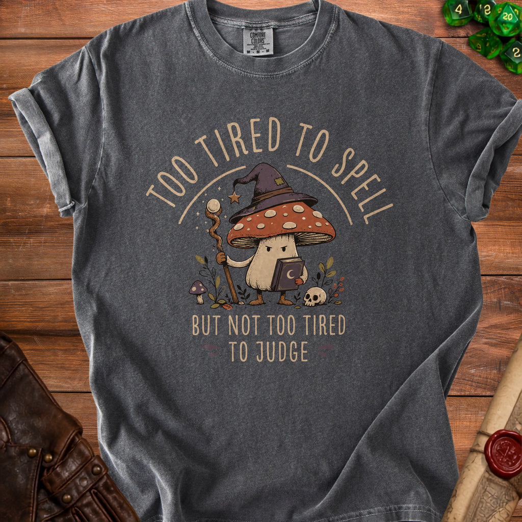 Dark grey t-shirt with graphic of a mushroom wizard, text "TOO TIRED TO SPELL BUT NOT TOO TIRED TO JUDGE".