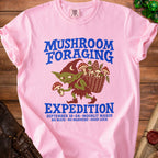 Pink t-shirt with a goblin holding mushrooms and text about mushroom foraging expedition.