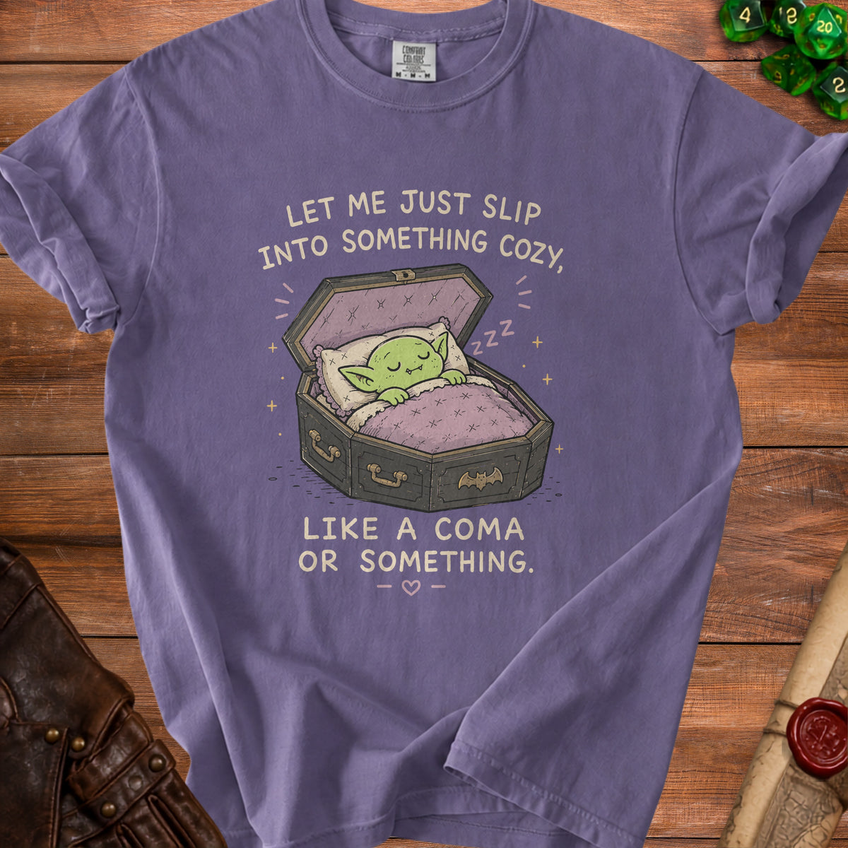 Purple t-shirt graphic of a green creature sleeping in an open coffin with text.