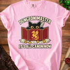 Pink t-shirt with a black cat holding a quill and a dragon shield; "Dungeon Master" and "It's All Canon Now".