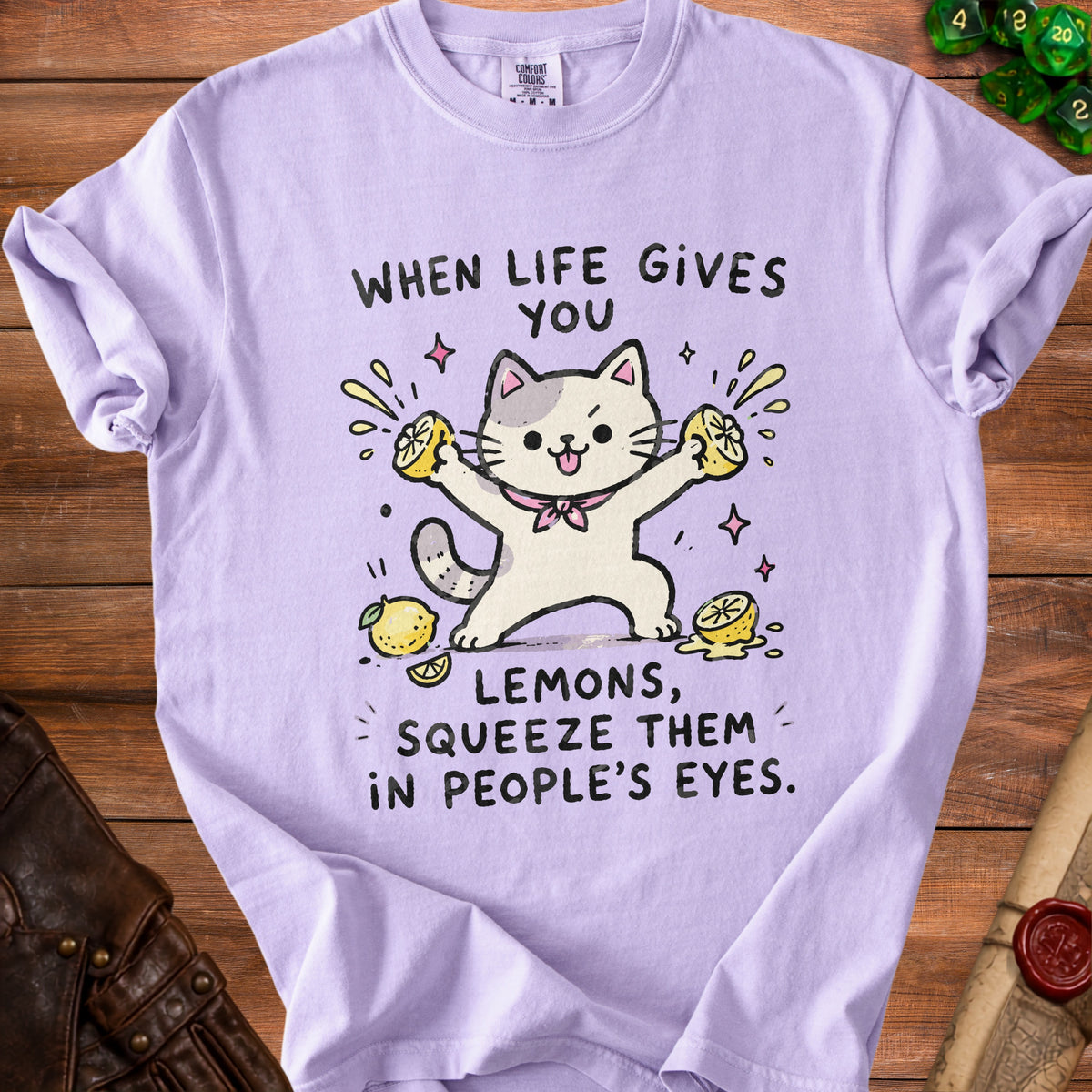 Light purple t-shirt with illustration of a cat squeezing lemons and text "When life gives you lemons, squeeze them in people's eyes."