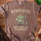 Brown t-shirt with a cartoon goblin holding a sword and shield, text "MICROPLASTICS ONLY MAKE ME STRONGER".
