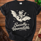 Black t-shirt with cream graphic of a cat in a wizard hat riding a bat, text "Socially Unavailable".
