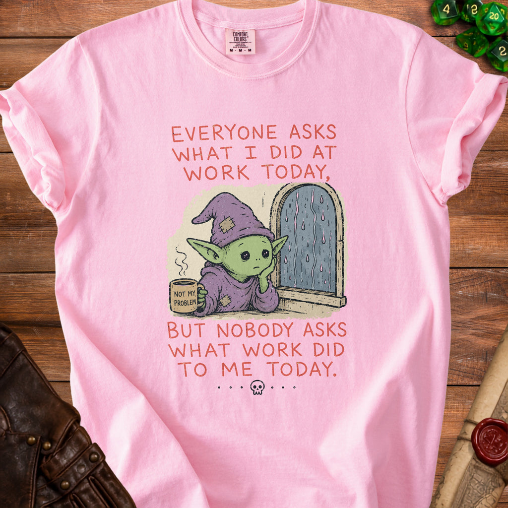 Pink t-shirt with a graphic of a creature holding a "Not My Problem" mug and text about work.