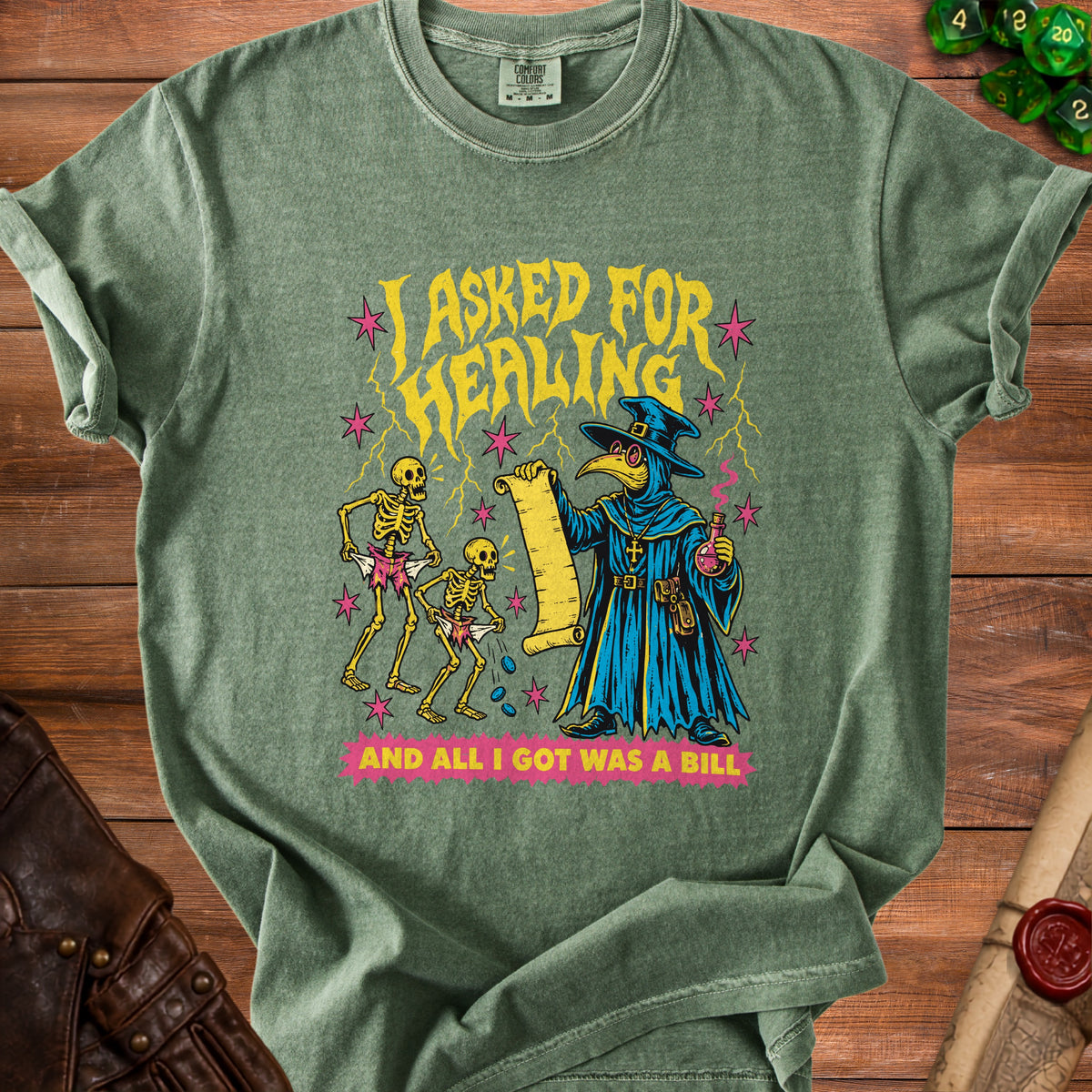 Green t-shirt with plague doctor, skeletons, and text "I ASKED FOR HEALING AND ALL I GOT WAS A BILL".