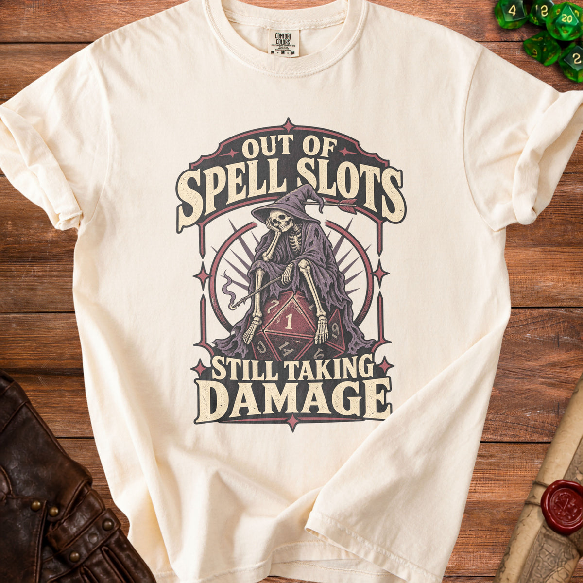 Cream t-shirt with a skeleton wearing a wizard hat and dice graphic, text "OUT OF SPELL SLOTS STILL TAKING DAMAGE."