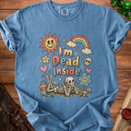 Blue t-shirt with graphic of skeleton lying in grass with sun, rainbow, and text "I'm Dead Inside".