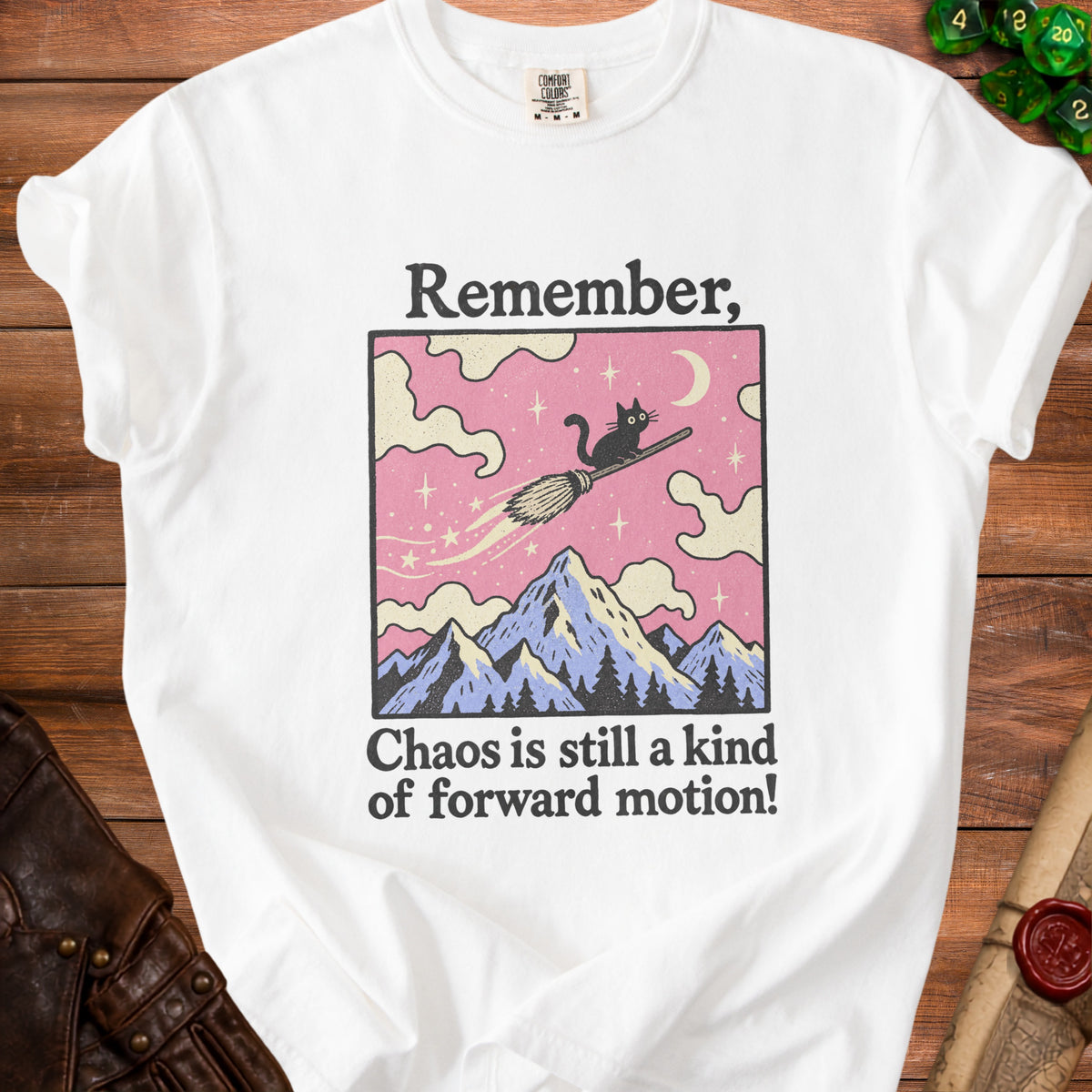White t-shirt with a graphic of a black cat flying on a broomstick over mountains, reading "Remember, Chaos is still a kind of forward motion!"