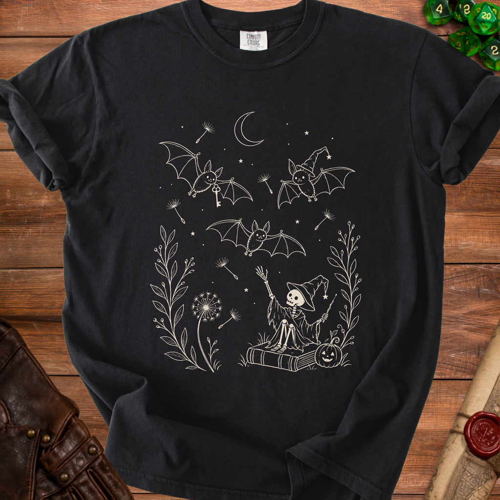 Black t-shirt with a white line drawing of a skeleton in a witch hat, bats, and dandelions.